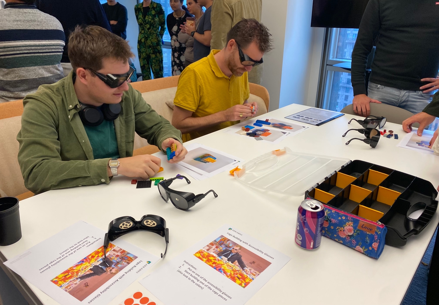Twee personen aan een bureau die legoblokken bouwen met een kleurenblindheidsbril.